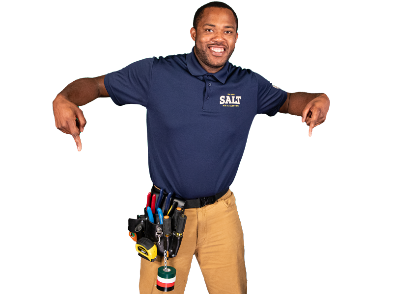 Smiling SALT technician in navy uniform pointing downward with both hands, wearing a tool belt with electrical tools