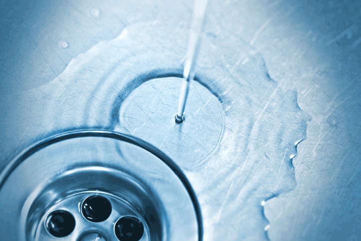 Close-up of water pouring into a metal sink drain with ripples and reflections