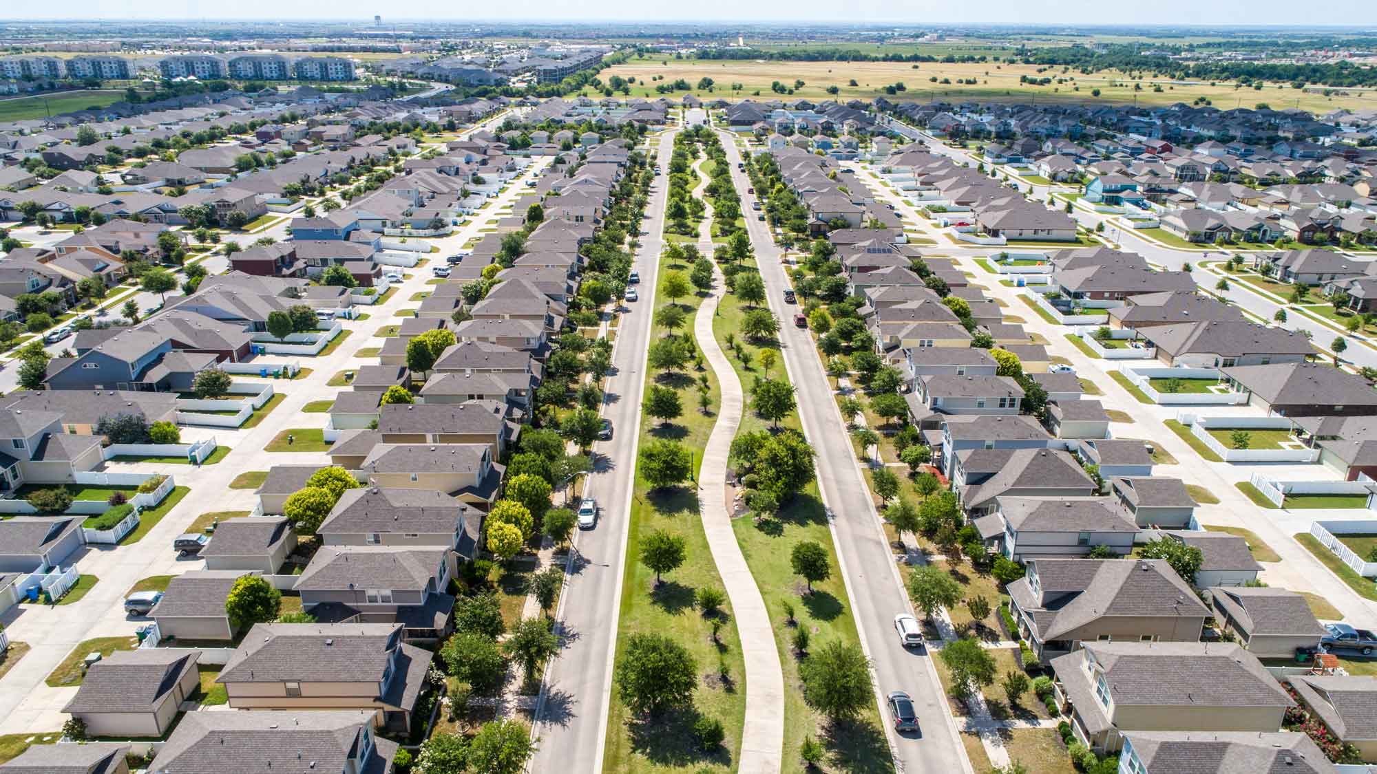 Aerial view of a residential neighborhood in Pflugerville, Texas, showcasing rows of modern homes with a landscaped greenbelt and walking path