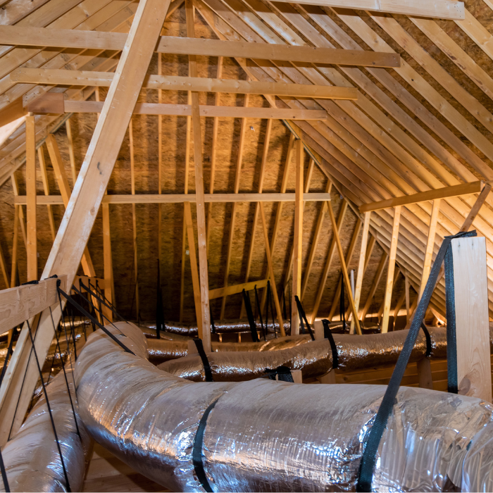Unfinished attic interior with exposed wooden framing and insulated HVAC ductwork running along the floor joists.