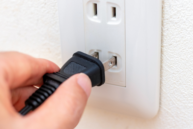 Close-up of a hand plugging a power cord into a wall outlet, showing an electrical connection being made.