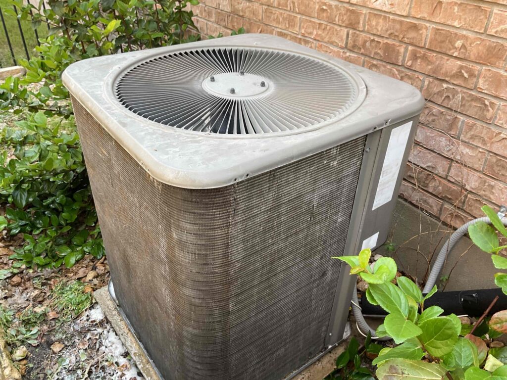 Aging outdoor AC condenser with dirty coils, showing signs a cooling system may be nearing failure.