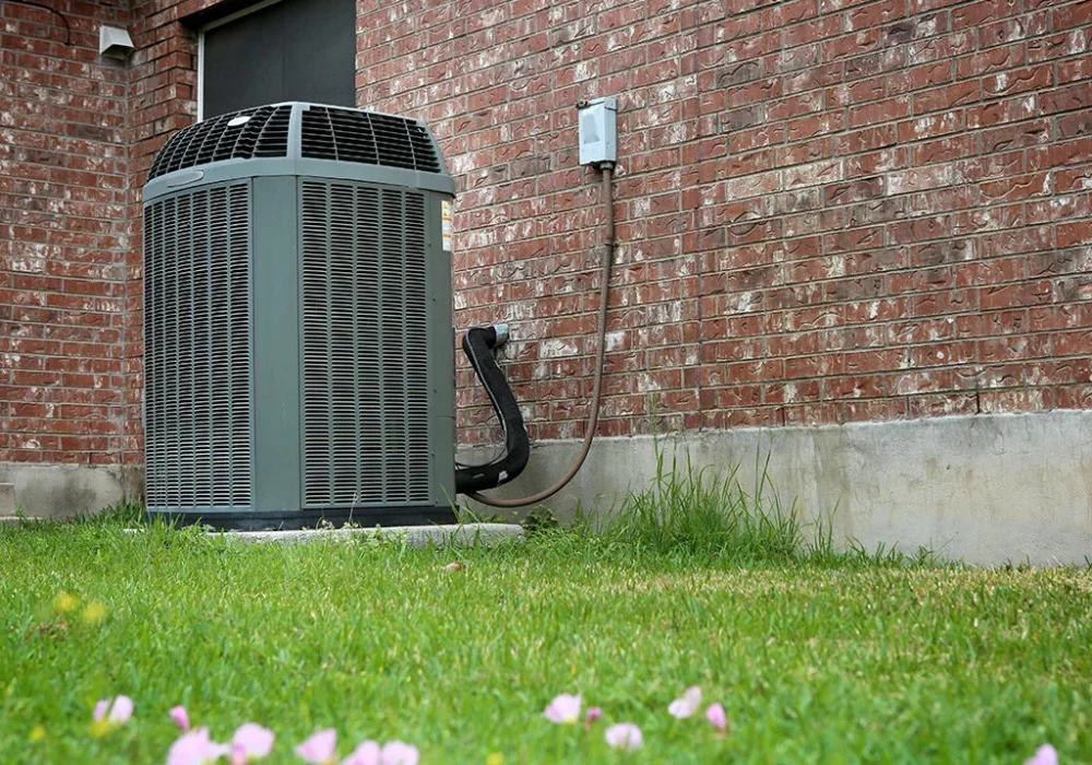 Outdoor central air conditioning unit installed on a concrete slab next to a brick home with electrical connection on the wall